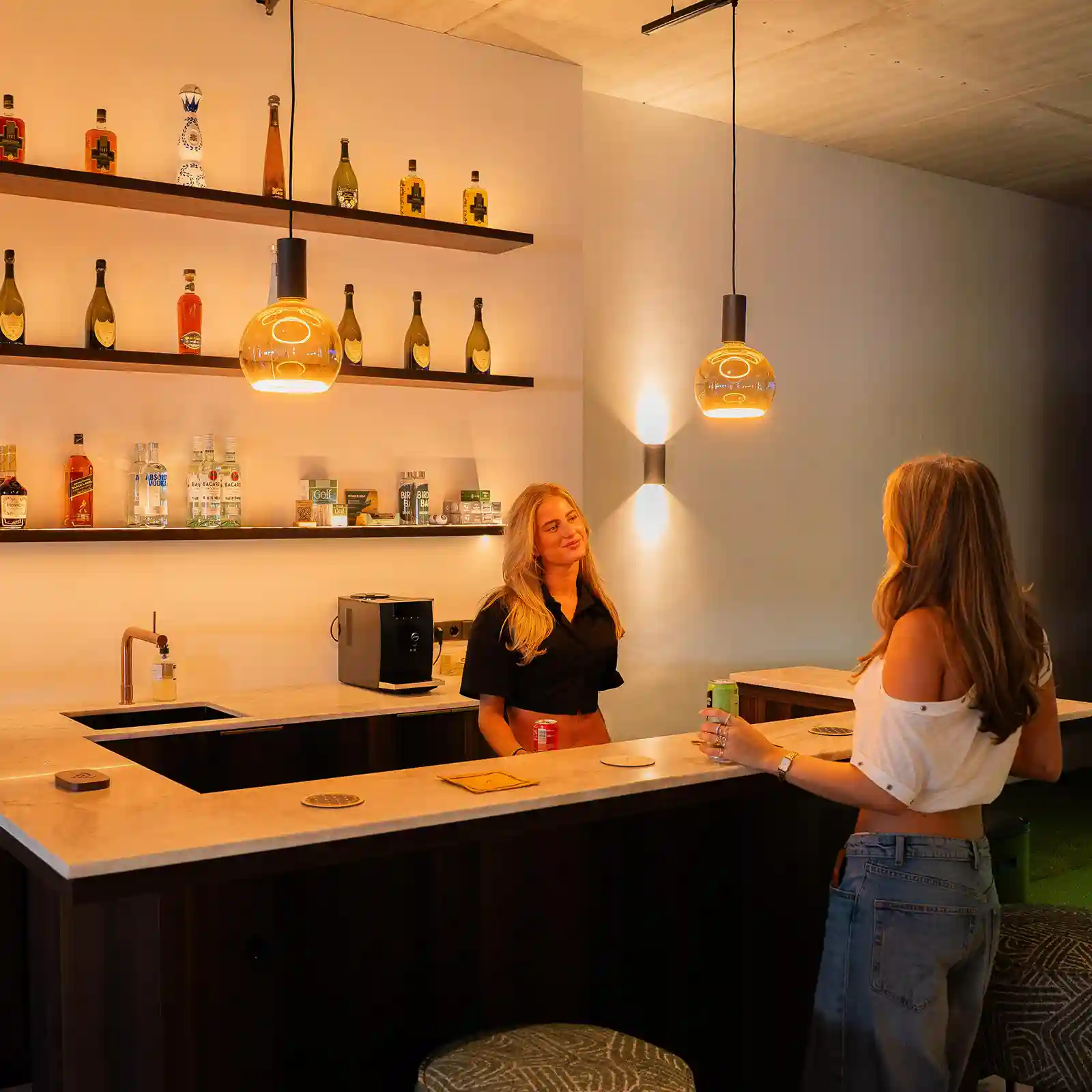 Twee bezoekers praten aan de warm verlichte bar van Birdie Bar